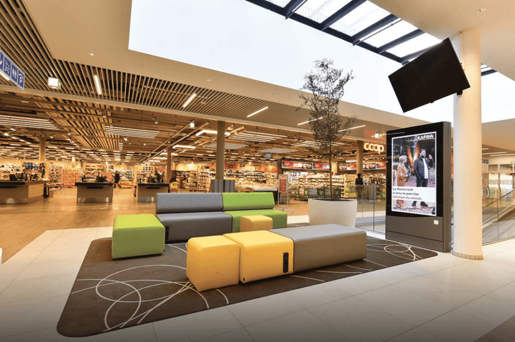 Zone de repos dans un centre commercial avec mobilier moderne, couleurs vives et atrium lumineux