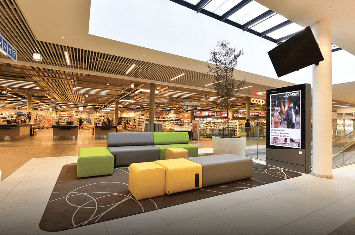 Zone de repos dans un centre commercial avec mobilier moderne, couleurs vives et atrium lumineux