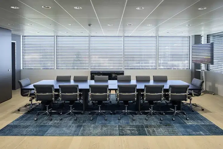 Une salle de réunion professionnelle avec une longue table de conférence entourée de chaises ergonomiques, située dans un environnement de bureau moderne avec de grandes fenêtres