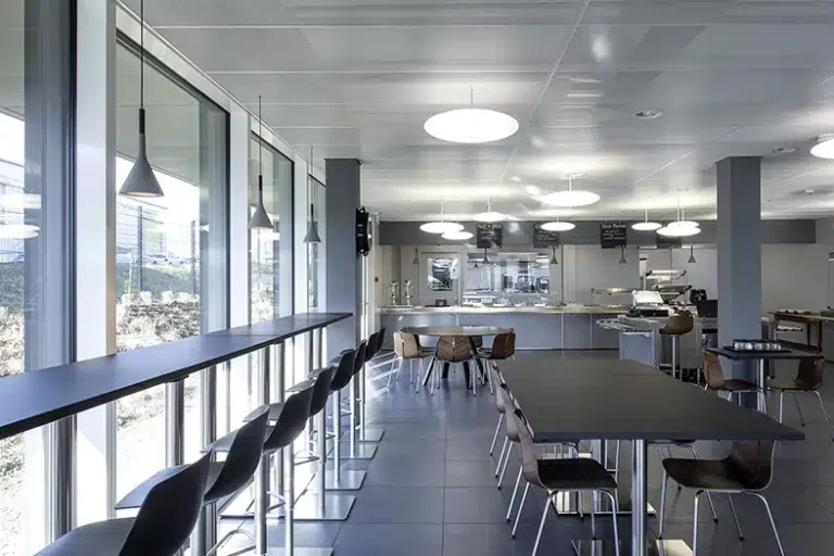 Un espace de restauration avec des tabourets hauts le long de fenêtres en verre et un éclairage suspendu moderne