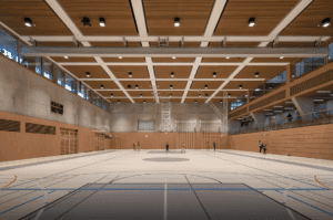 Une grande salle de sport intérieure avec un plafond en bois doté d’un éclairage intégré, un terrain de basketball et des structures d’escalade