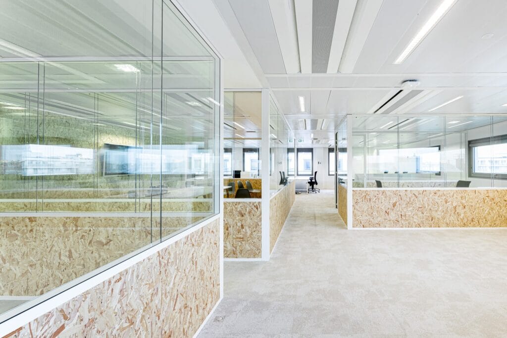 Bureau en concept ouvert avec des cloisons en verre et des panneaux en bois OSB, offrant un espace de travail contemporain et durable