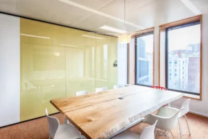 alle de réunion élégante avec une grande table en bois naturel, des chaises blanches et une paroi vitrée offrant un espace de travail moderne
