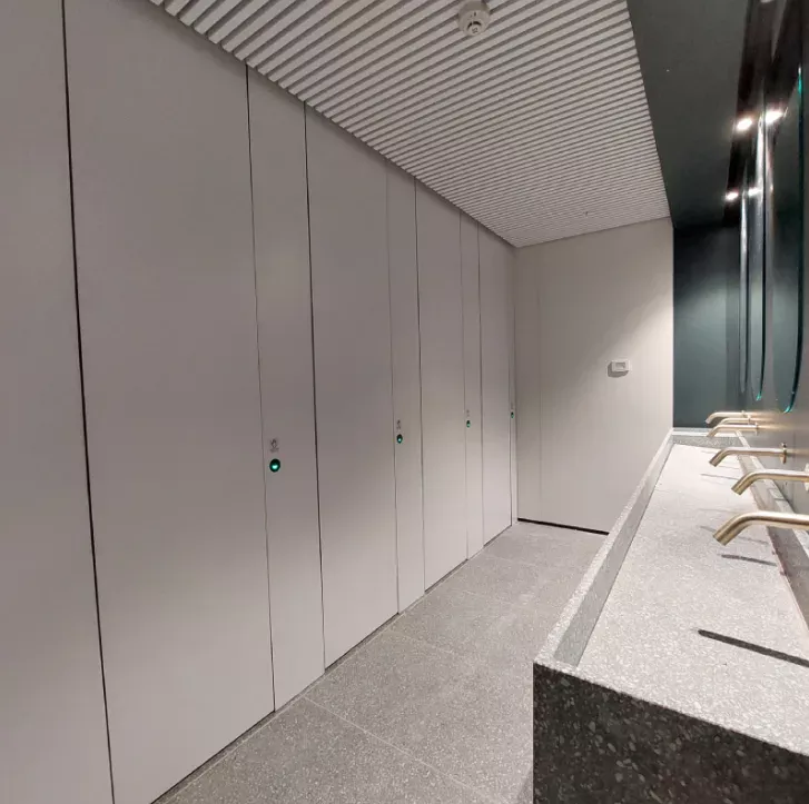 Toilettes modernes avec des éléments de design linéaire, des cabines grises, un lavabo en pierre et des miroirs intégrés