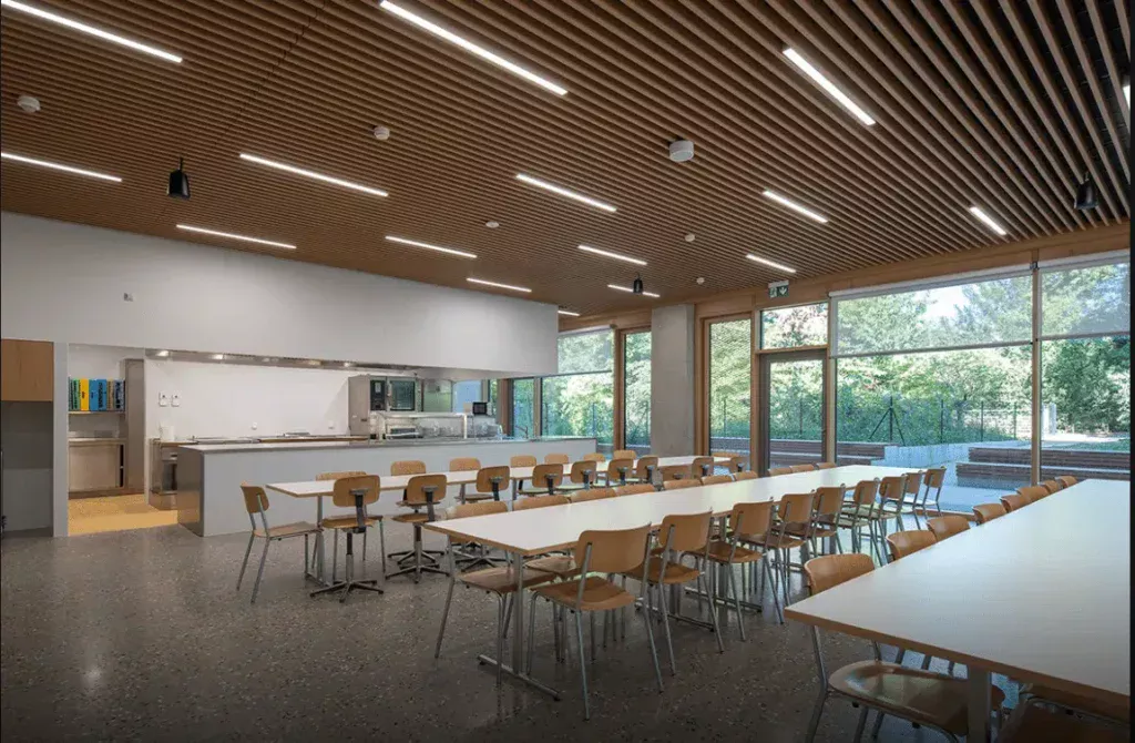 Cafétéria spacieuse avec plafond en lattes de bois, grandes fenêtres et mobilier minimaliste