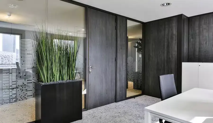 Un bureau privé avec un revêtement en bois foncé, des cloisons vitrées givrées avec un motif de skyline et un bureau moderne