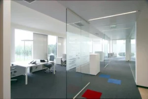 Un espace de bureau lumineux et ouvert avec des bureaux blancs et des cloisons vitrées du sol au plafond, ornées de lignes givrées pour plus de confidentialité