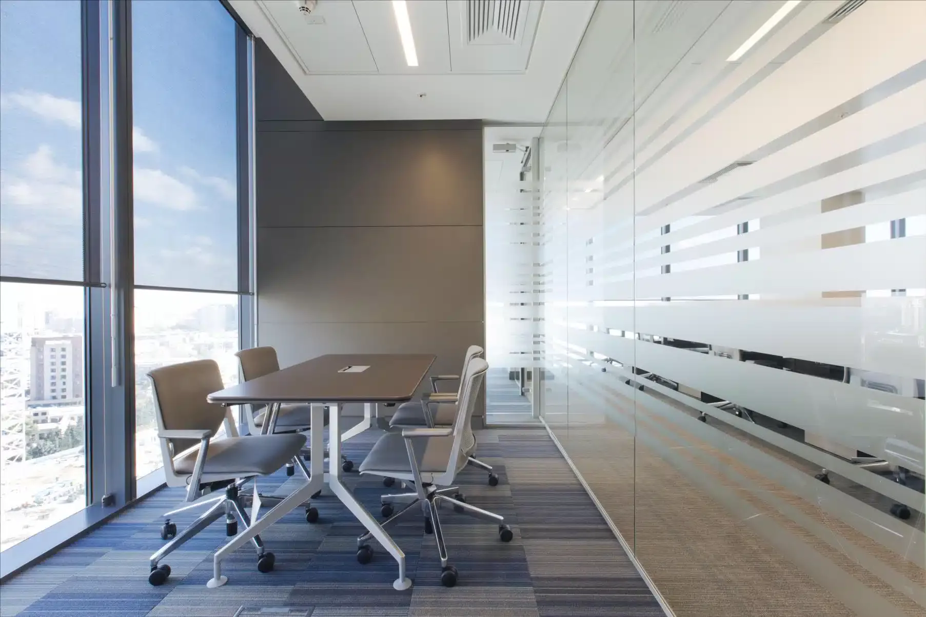Une salle de conférence moderne avec une table élégante et des chaises ergonomiques, dotée d'une grande cloison vitrée avec des bandes givrées pour plus d'intimité