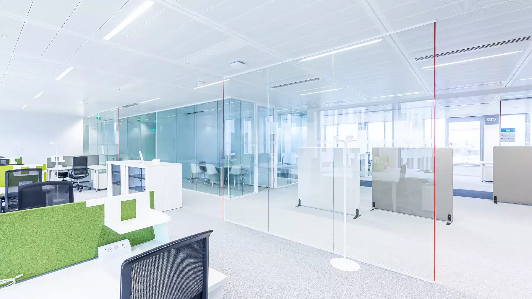 Un bureau high-tech avec des cabines vitrées, du mobilier blanc et des séparateurs verts pour un look frais et moderne