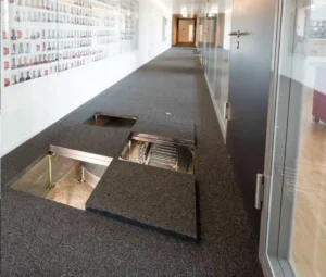 Un système de plancher technique dans un couloir de bureau moderne, avec des panneaux amovibles révélant les câblages et équipements en dessous