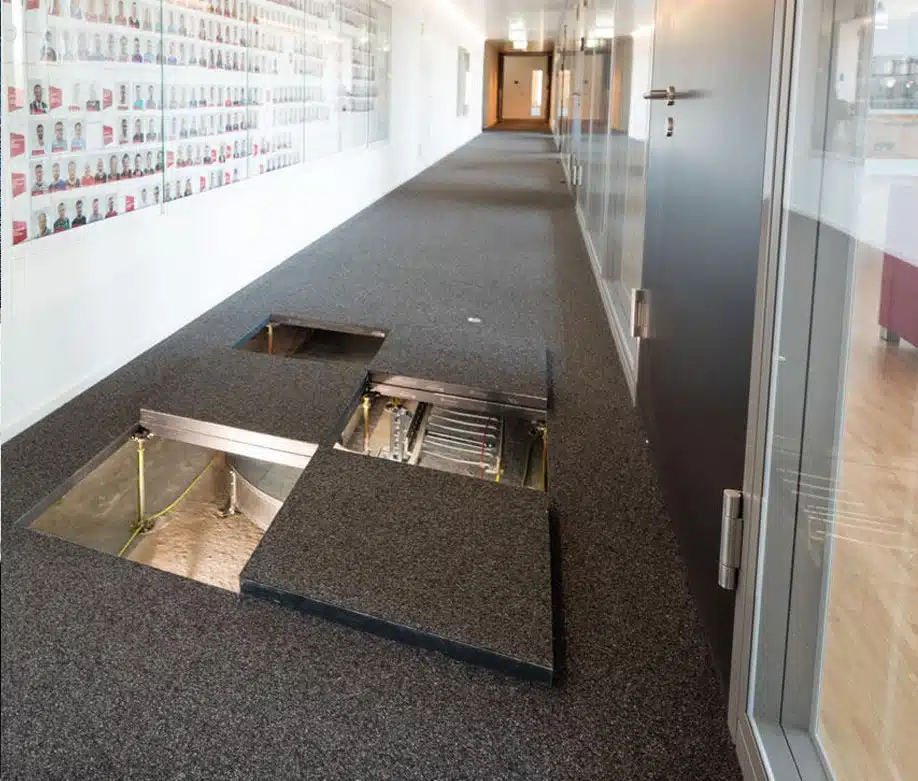 Un système de plancher technique dans un couloir de bureau moderne, avec des panneaux amovibles révélant les câblages et équipements en dessous