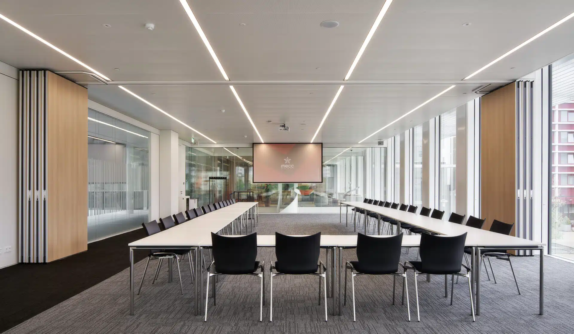 Salle de conférence spacieuse avec des cloisons en verre, un éclairage moderne et un écran de projection, offrant un environnement de réunion professionnel et lumineux