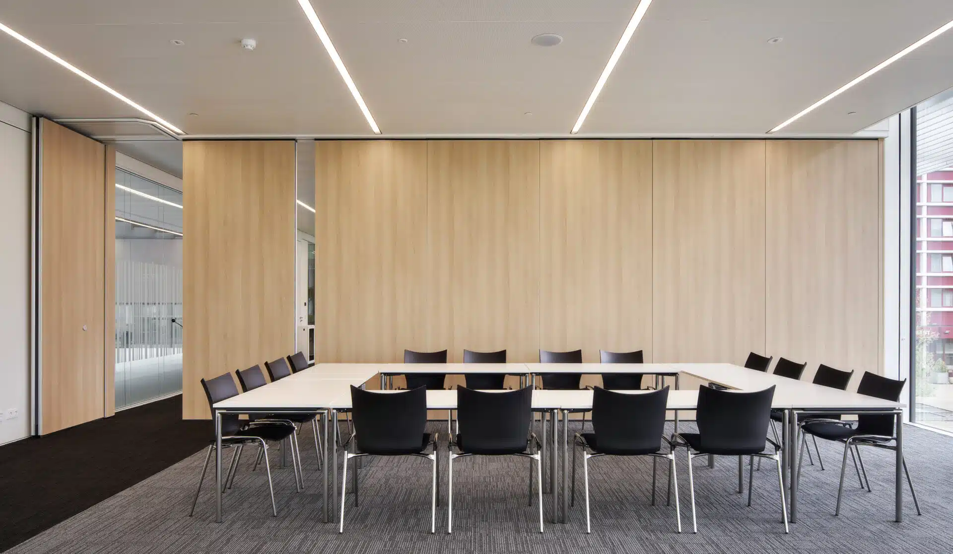 Une salle de réunion professionnelle avec une cloison en bois, des chaises noires et une disposition structurée de la table de conférence