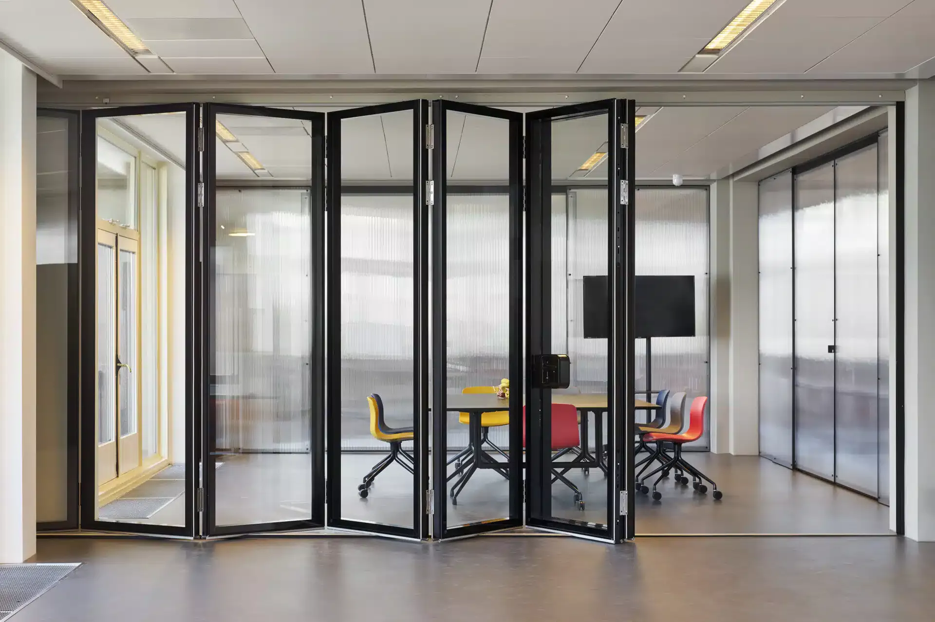 Salle de réunion avec une cloison en verre partiellement repliée, offrant une division flexible de l’espace tout en maintenant la transparence et la luminosité