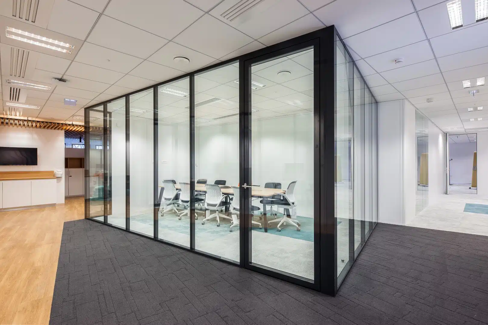Salle de réunion transparente avec des murs en verre et des cadres noirs, permettant à la lumière naturelle de circuler dans l’espace