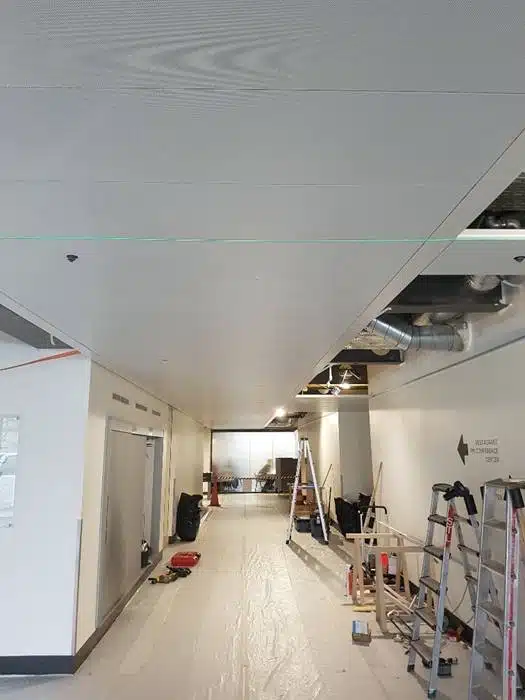 Installation de panneaux de plafond en cours dans un espace commercial, avec un plafond de style industriel et des conduits apparents