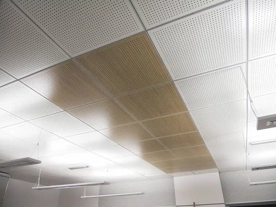 Plafond suspendu avec un mélange de panneaux métalliques perforés et de finitions en bois, améliorant la performance acoustique et l’esthétiqu