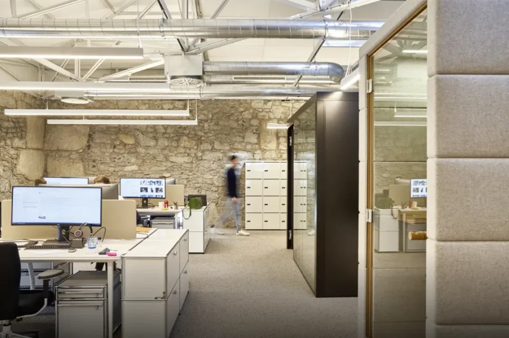 Espace de bureau ouvert avec des murs en pierre apparente, des bureaux modernes et des conduits d'air visibles pour un style industriel