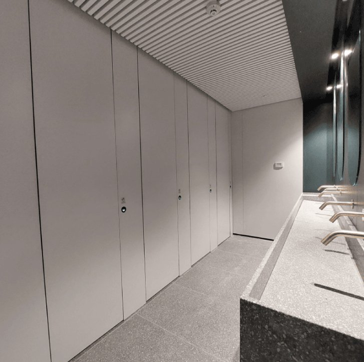 Toilettes modernes avec des éléments de design linéaire, des cabines grises, un lavabo en pierre et des miroirs intégrés