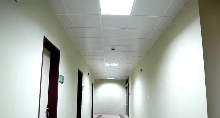 Long couloir de bureau avec un plafond suspendu en grille, éclairage encastré et murs de couleur neutre