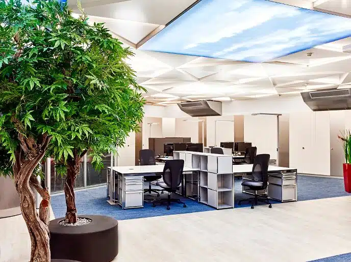 Intérieur de bureau contemporain avec espaces de travail ouverts, arbres d'intérieur et plafond lumineux simulant le cie