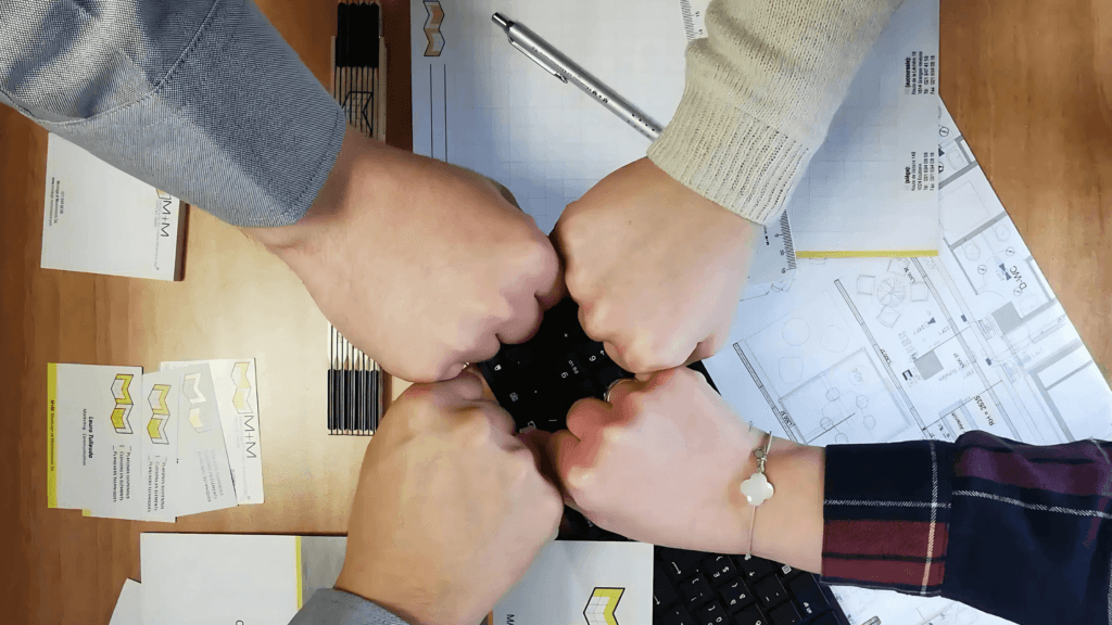 Gros plan de plusieurs mains en geste de solidarité, symbolisant le travail d’équipe et la collaboration sur un projet architectural