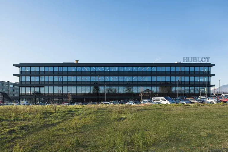 Fa&ccedil;ade ext&eacute;rieure du b&acirc;timent de l&rsquo;entreprise Hublot avec vitres noires et voitures gar&eacute;es devant