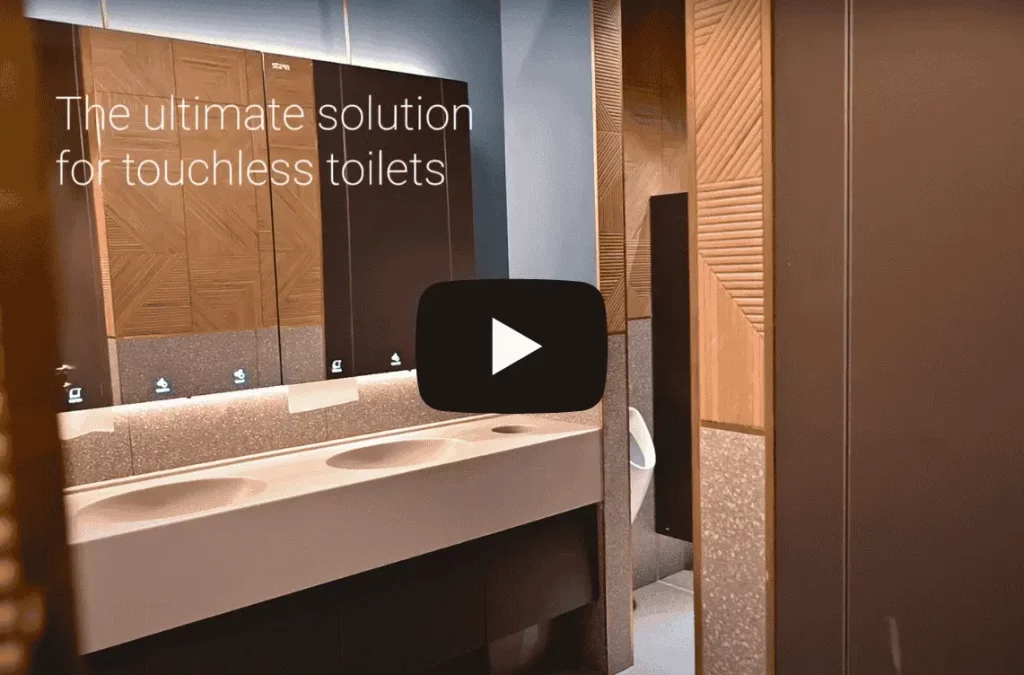 Toilettes publiques modernes avec lavabos sans contact et décoration en panneaux de bois, comprenant des miroirs et un comptoir élégant. Le texte indique : 'La solution ultime pour des toilettes sans contact.' Une icône de lecture indique une miniature vidéo