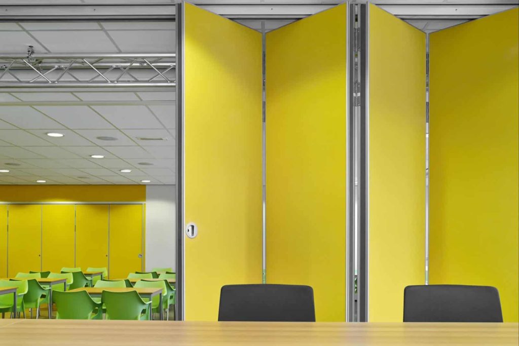 Cloison mobile jaune dans une salle de réunion moderne avec des chaises vertes et une table en bois, démontrant la flexibilité et les solutions acoustiques
