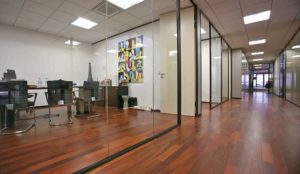 Couloir de bureau avec cloisons vitrées toute hauteur et salles de réunion privées sur parquet