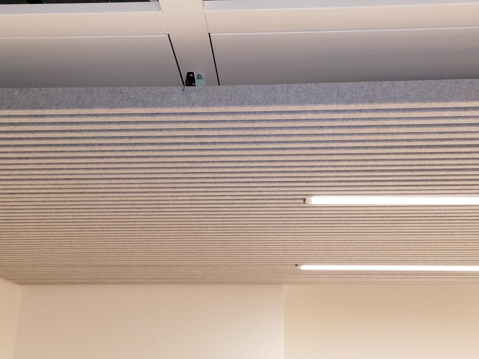 Plafond suspendu acoustique moderne avec lames linéaires et éclairage LED intégré, idéal pour l'isolation phonique et le design esthétique de bureaux.
