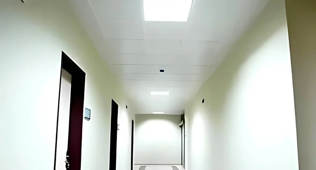 Long couloir de bureau avec un plafond suspendu en grille, éclairage encastré et murs de couleur neutre