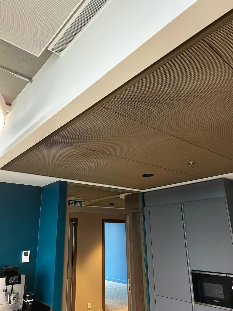 Panneaux acoustiques perfor&eacute;s au plafond dans une kitchenette de bureau moderne avec &eacute;clairage int&eacute;gr&eacute; et mur bleu