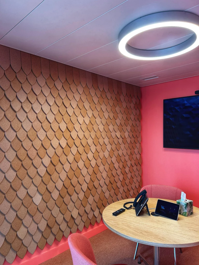 Salle de r&eacute;union avec panneaux muraux acoustiques en li&egrave;ge, luminaire circulaire et table ronde en bois