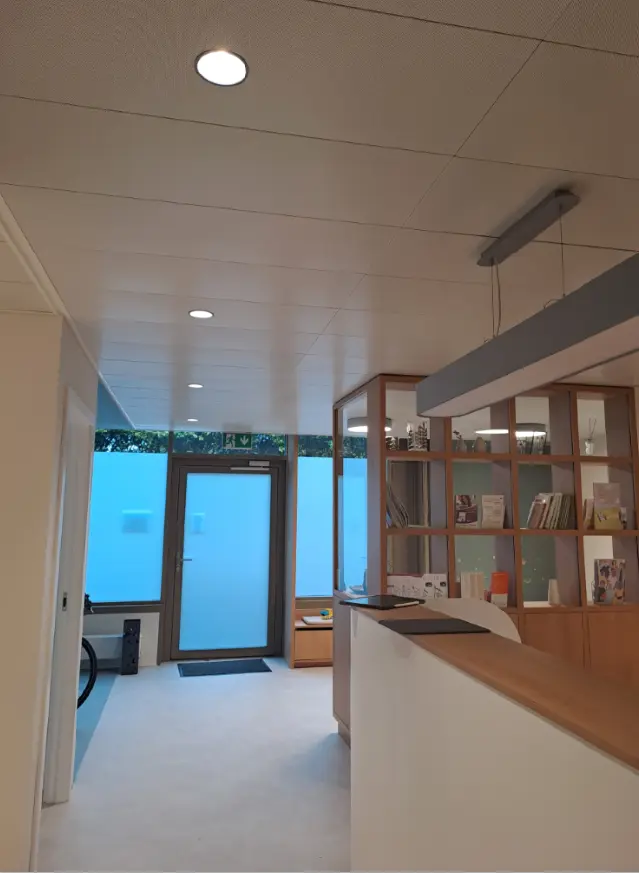 Espace d&rsquo;accueil avec plafond acoustique perfor&eacute;, porte d&rsquo;entr&eacute;e en verre d&eacute;poli et &eacute;tag&egrave;res en bois