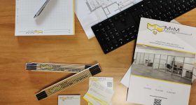 Bureau avec de la papeterie de marque, des plans architecturaux et une brochure marketing de M+M Montage et Maintenance