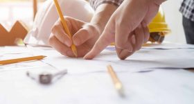 Gros plan de deux personnes pointant des plans de construction, entourées d'outils et de casques